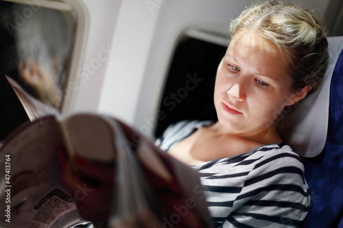 Photo: Young beautiful woman reads magazine in airplanee Young beautiful woman reads magazine in airplanee