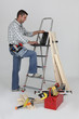 Carpenter using a laptop whilst stood by ladder