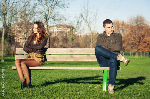 Photo: Angry young couple sitting away outdoors on a bench. Angry young couple sitting away outdoors on a bench.