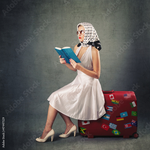 Photo: Retro woman with sunglasses and suitcase reading book Retro woman with sunglasses and suitcase reading book