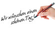 Hand mit Stift schreibt Wir wünschen einen schönen Tag