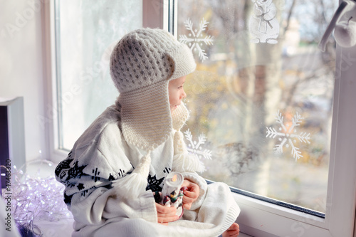 Photo: winter boy sitting by the window in a white knitted cap winter boy sitting by the window in a white knitted cap