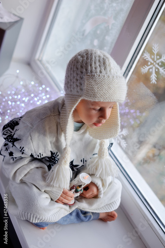 Photo: winter boy sitting by the window in a white knitted cap winter boy sitting by the window in a white knitted cap
