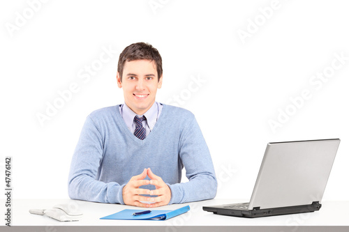 Photo: Smiling male posing on a desk with laptop and other office staff Smiling male posing on a desk with laptop and other office staff