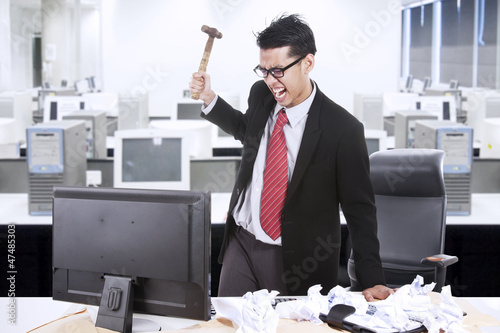 Photo: Angry businessman throw hammer at computer Angry businessman throw hammer at computer