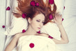 Beautiful red-haired girl in bed with rose petal. Studio shot.