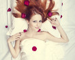Beautiful red-haired girl in bed with rose petal. Studio shot.