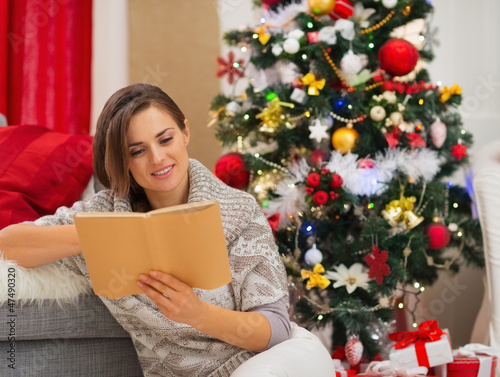 Photo: Young woman reading book near Christmas tree Young woman reading book near Christmas tree