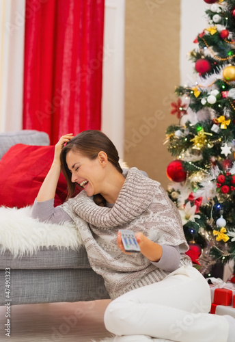 Photo: Laughing young woman watching TV near Christmas tree Laughing young woman watching TV near Christmas tree