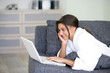 Foto: Woman lying on a sofa and using her laptop Woman lying on a sofa and using her laptop
