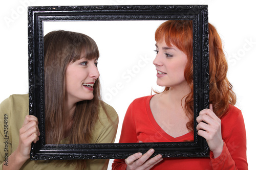 Photo: Two women poking heads though empty picture frame Two women poking heads though empty picture frame