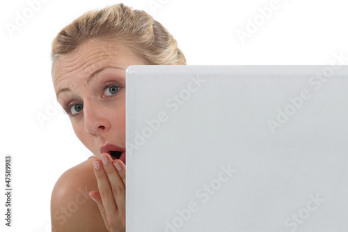 Photo: Surprised woman peering out from behind her laptop Surprised woman peering out from behind her laptop
