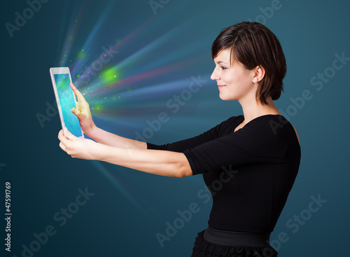 Photo: Young woman looking at modern tablet with abstract lights Young woman looking at modern tablet with abstract lights