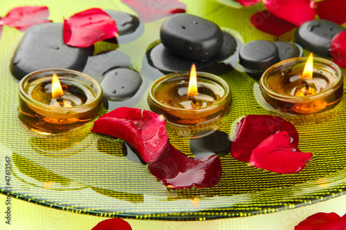 Photo: spa stones with rose petals and candles in water on plate spa stones with rose petals and candles in water on plate
