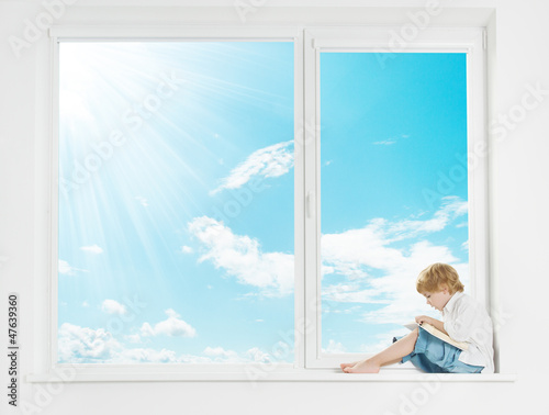 Photo: Window sunshine sky. Child on windowsill reading book. Window sunshine sky. Child on windowsill reading book.