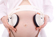 Hands of pregnant woman in white holding white headphones