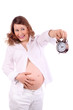 Pregnant woman in white holds at arm alarm clock