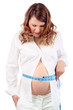 Dissatisfied pregnant woman in white measures belly