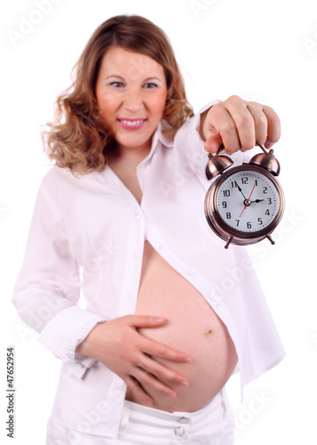 Photo: Dissatisfied pregnant woman in white holds at arm alarm clock Dissatisfied pregnant woman in white holds at arm alarm clock