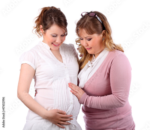 Photo: Pregnant woman in white and her girlfriend touching her stomach Pregnant woman in white and her girlfriend touching her stomach