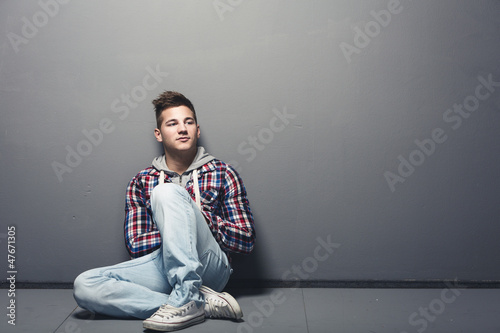 Photo: Jugendlicher sitzt angelehnt an eine Wand Jugendlicher sitzt angelehnt an eine Wand