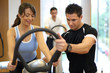 Personal trainer explaining a vibration plate in a gym to a fema