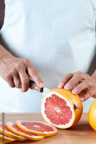 Photo: Vertical shot of female hands slicing a fresh grapefruit Vertical shot of female hands slicing a fresh grapefruit
