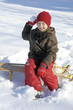 Kind auf Schlitten im Schnee wirft Schneeball