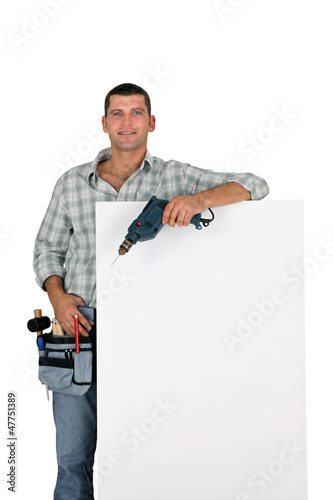 Photo: Builder with power drill stood by blank poster Builder with power drill stood by blank poster