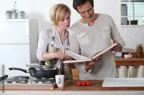 Photo: Couple cooking together with a recipe book Couple cooking together with a recipe book