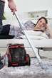 Photo: A man vacuuming while his girlfriend is reading a book. A man vacuuming while his girlfriend is reading a book.