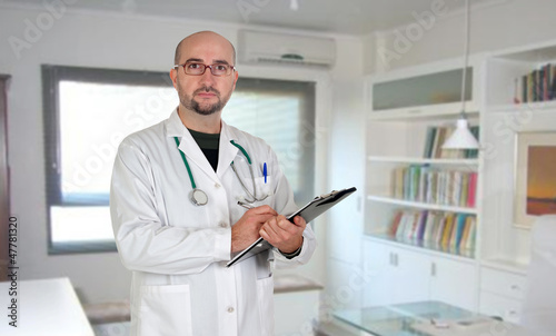 Photo: Doctor with clipboard and paperwork in his office Doctor with clipboard and paperwork in his office