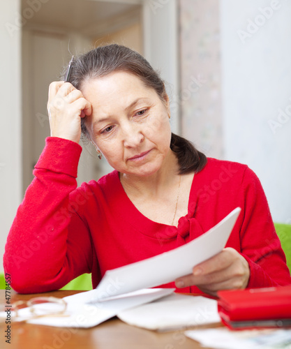 Photo: serious mature woman reads payments at home serious mature woman reads payments at home