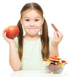 Little girl choosing between apples and sweets