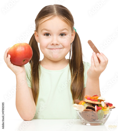 Photo: Little girl choosing between apples and sweets Little girl choosing between apples and sweets