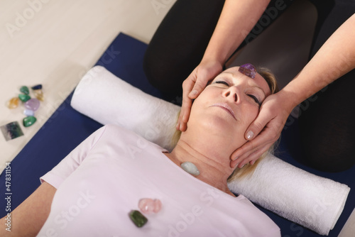 Photo: Young therapist arranging crystals on female client for reiki th Young therapist arranging crystals on female client for reiki th