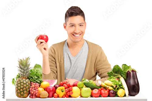 Photo: Handsome guy holding an apple on a table full of various food Handsome guy holding an apple on a table full of various food