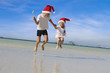 two young happy children kids in santa hats jumping on beach on