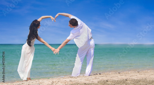 Photo: young couple making heart by arms on beach young couple making heart by arms on beach