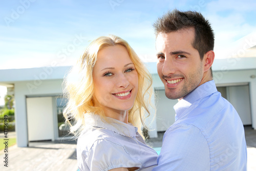 Photo: Cheerful couple standing in front of modern house Cheerful couple standing in front of modern house