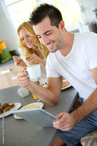 Photo: Young man sitting in home kitchen with tablet Young man sitting in home kitchen with tablet