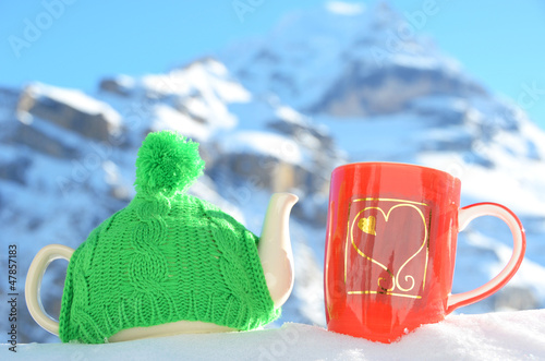 Photo: Tea pot in the cap and a cup against alpine scenery Tea pot in the cap and a cup against alpine scenery