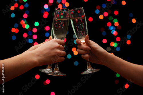 Photo: woman hand with glasses of champagne, on garland background. woman hand with glasses of champagne, on garland background.