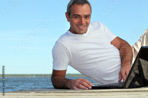 Photo: Man looking his laptop by the lake Man looking his laptop by the lake