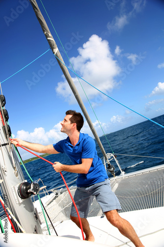 Photo: Young man lifting the sail of catamaran during cruising Young man lifting the sail of catamaran during cruising