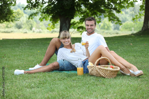 Photo: Young couple having a picnic in a meadow Young couple having a picnic in a meadow