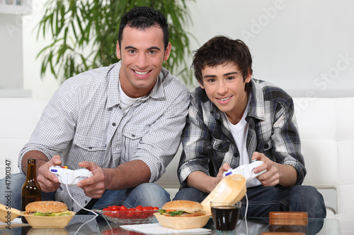Photo: Father and son playing video games and eating junk-food Father and son playing video games and eating junk-food