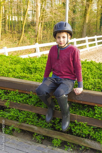 Photo: cute teenage boy in helmet and boots for horse riding sitting n cute teenage boy in helmet and boots for horse riding sitting n