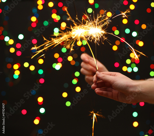 Photo: beautiful sparklers in woman hands on garland background. beautiful sparklers in woman hands on garland background.