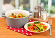 Vegetable stew in gray pot on wooden table on bright background